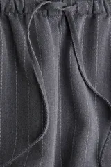 Pantalón gris oscuro a rayas verticales finas, de corte holgado, con elástico y cordón ajustable en la cintura, bolsillos laterales y bolsillos decorativos en la parte trasera. Confeccionado en sarga.