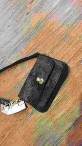 Minibag tipo acordeón, color negro con acabado brillante o glitter. Presenta solapa frontal con cierre metálico dorado de giro. Incluye correa larga ajustable y correa corta de mano.