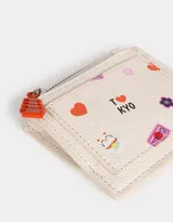 Monedero de cuerina color crudo con cierre superior, bolsillo frontal estampado con motivos japoneses y dije colgante de pagoda roja.