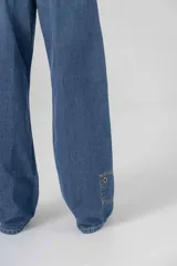 Pantalón de jean azul, corte recto y extra largo, con aplique de denim y ojalillo en una pierna.
