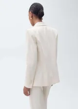 Blazer color crema con cuello de solapa, cierre cruzado con doble botonadura y corte recto.