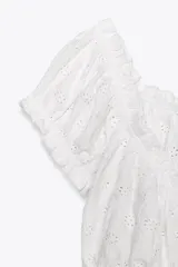 Top crop blanco de escote cuadrado y manga corta abullonada. Detalle de lazada en el pecho y volantes en el escote y el bajo.