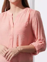 Blusa blanca de gasa marca Zac & Rachel, con cuello a la base, escote en V, abertura central con botones, bolsillo aplicado en el pecho y mangas largas regulables con presilla y botón. Tiene terminación opcional de nudo en el ruedo.