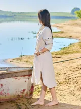 Vestido camisero largo de lino color beige, con cuello clásico, manga larga con puños abotonados y cierre frontal con botones. Tiene un bolsillo de parche en el pecho.