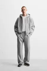 Sudadera negra relaxed fit de algodón compacto con interior en rizo, cuello con capucha ajustable, manga larga, bolsillos frontales tipo canguro, acabados en rib y cierre frontal con cremallera.