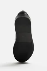 Zapato de vestir tipo derby de cuero negro, con puntera lisa, horma redonda y suela con ligero tacón.