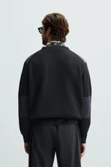 Jersey negro de punto con cuello redondo y manga larga. Presenta parches combinados en hombros y codos.