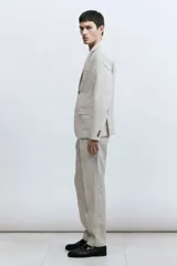 Pantalón de traje de lino color beige, corte slim fit, con cierre y corchete oculto, bolsillos laterales y traseros ribeteados.