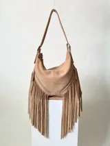Bolso bandolera de cuero color beige con flecos largos en la parte inferior y dos bolsillos frontales con cierre.
