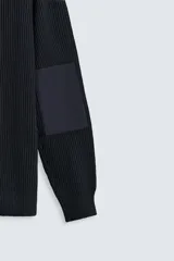Jersey negro de punto con cuello redondo y manga larga. Presenta parches combinados en hombros y codos.