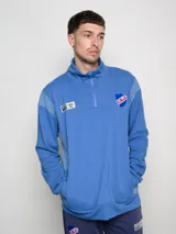 Buzo azul de felpa con medio cierre, cuello alto y mangas largas. Presenta el escudo del Club Nacional de Football en el pecho y el logo de Umbro en la manga.