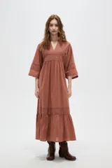 Vestido largo color marrón, con escote en V, mangas 3/4 y detalles de broderie en el pecho, mangas y falda. La falda tiene un volado en el ruedo.