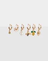 Set de tres pares de aros argolla dorados con distintos dijes colgantes: cristal amarillo, flor esmaltada blanca, perla con forma de corazón, abeja esmaltada, limón con cristales y frutilla.