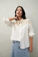 Camisa de lino color crudo y beige, con diseño bicolor y recorte ondulado en el canesú. De silueta relajada, cuenta con mangas amplias y puños camiseros. Se completa con botones de nácar.