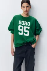 Buzo verde con cuello redondo, puños y bajo acanalados. Estampado frontal con la palabra "SOHO" y el número "95" en color blanco.