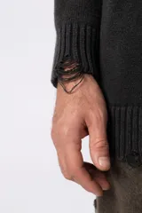 Sweater de punto grueso color gris oscuro con cuello redondo y mangas largas. Presenta un diseño de texto bordado en el frente y detalles de roturas en los puños y el ruedo.