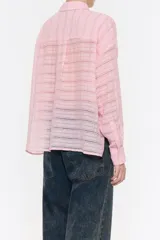 Camisa rosa con rayas horizontales, de corte holgado, manga larga con puños abotonados, cuello camisero, cierre frontal con botones, bolsillo de parche en el pecho y canesú en la espalda con pliegue.