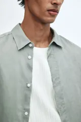 Camisa de lino color gris con cuello inglés, tapeta clásica, canesú en la espalda, mangas largas con tapeta de manga y botón, cierre ajustable de botón en los puños y bajo redondeado.
