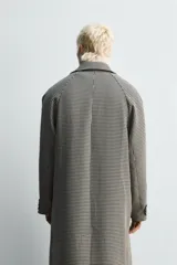 Abrigo largo de corte recto con estampado de cuadros en blanco y negro. Tiene cuello solapa, manga larga, bolsillos laterales y cierre frontal con botones.
