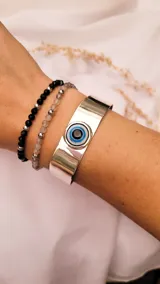 Brazalete rígido plateado con un dije de ojo turco en el centro.