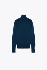 Jersey negro de punto liso con cuello alto, manga larga y detalle de botones dorados en los puños.