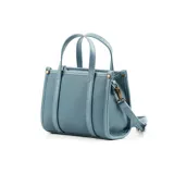 Cartera tote mini color celeste de cuero sintético con textura granulada. Tiene doble asa corta, correa larga regulable y extraíble, cierre superior y herrajes plateados. El frente está adornado con el logo metálico de la marca.