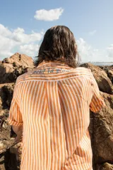 Camisa de lino a rayas verticales color naranja y blanco, de manga corta y corte oversize. Presenta bordados con motivos playeros en el frente y la espalda.