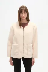 Chaqueta corta de tejido bouclé o pelo sintético color crema, con cuello redondo, cierre frontal metálico y dos bolsillos frontales amplios.