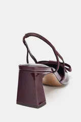 Zapato destalonado de mujer, color borgoña (vino), con acabado acharolado y punta fina. Presenta un lazo de tela en la parte delantera y una tira fina en el talón. El tacón es ancho y de altura media.