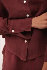 Camisa de lino color vino tinto, con cuello mao y botones blancos. Presenta un corte holgado y manga larga con puños abotonados.