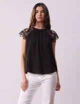 Blusa negra de crepe con apliques de crochet en los hombros. Tiene cuello redondo, mangas cortas y espalda con abertura ojal y botones.