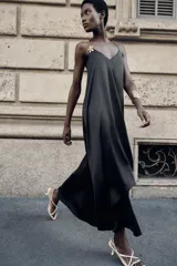 Vestido midi negro de satén con escote en pico, tirantes finos y aplique dorado con cadena en el hombro.