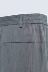 Pantalón cargo gris con textura acanalada, corte relaxed fit, cintura elástica con pliegues frontales, bolsillos laterales tipo cargo con solapa, bolsillos frontales y traseros de vivo, cierre frontal con cremallera y botón.