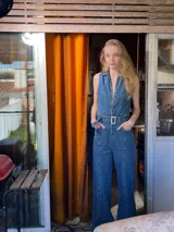 Enterito denim azul con corte holgado, recto de pierna y entallado de tronco, con cinturón ajustable. La parte de arriba cuenta con cierre hasta el final, terminado en cuello camisero.