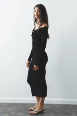 Vestido largo de punto negro con escote recto, hombros descubiertos, mangas largas y detalle de pieza metálica en el delantero.