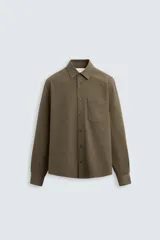 Camisa color verde oliva de corte relaxed fit, confeccionada en tejido de algodón con acabado cepillado. Tiene cuello solapa, manga larga con puño abotonado, bolsillo de parche en el pecho, efecto lavado y cierre frontal con botones.