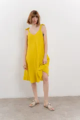 Vestido corto amarillo de lino, con escote en V y tirantes finos con detalle de moño en los hombros.