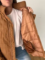 Campera color camel de corte relajado, con exterior de tejido efecto gamuza e interior acolchado. Tiene cuello alto, cierre frontal con cremallera, bolsillos laterales y bolsillo interno.
