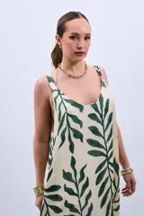 Vestido largo color crudo con estampado de hojas verdes, de corte amplio y breteles finos.