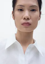 Camisa blanca de manga corta confeccionada en mezcla de algodón y lino, con cierre frontal de botones, cuello camisero y corte recto.