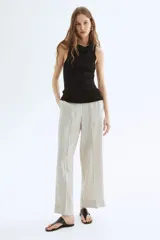 Pantalón ancho de tiro alto con elástico en la parte posterior de la cintura y cierre oculto con corchete en un lado. Bolsillos laterales discretos y piernas amplias con pliegues adelante y atrás. Diseño a rayas verticales grises y blancas.