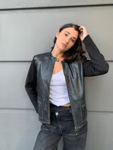 Campera negra con cuerpo de cuero sintético y mangas largas de tejido de punto fino. Presenta cierre frontal con cremallera, cuello redondo y bolsillos con cierre en el frente. Detalles de costuras en color blanco.