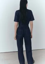 Mono largo de denim azul oscuro, con cuello camisero, mangas cortas y cierre frontal con cremallera. Incluye cinturón ajustable, bolsillos laterales y trabillas.