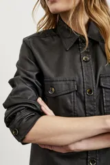 Sobrecamisa negra de textura simil cuero, con cuello camisero, cierre frontal con botones, mangas largas con puños abotonados, dos bolsillos con solapa en el pecho y corte recto.