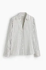 Blusa de manga larga a rayas verticales blancas y negras, con cuello clásico, escote en V y cierre frontal con botones. Puños con detalle de rayas horizontales y bajo redondeado.