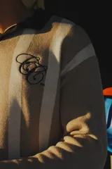 Sweater de punto a rayas verticales azules y blancas, con cuello polo negro y logo bordado en el pecho.