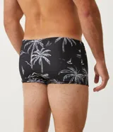 Sunga de poliéster con cintura elástica y cordón interno para ajuste. Presenta un estampado tropical con palmeras, montañas y veleros en blanco sobre fondo negro.