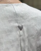 Blusa color rosa pálido de lino con bordados de motivos marinos, escote en V, mangas cortas abullonadas y cierre frontal con botones.