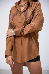 Camisa marrón de manga larga con detalles de lentejuelas y bordados en el frente. Tiene cuello clásico y botones frontales.