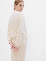 Buzo deportivo Gap color crema, con cuello redondo, mangas largas abullonadas y puños ajustados. Tiene el logo "GAP" bordado en negro en el pecho.